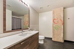 Un baño moderno con un lavamanos blanco, armarios de madera, un espejo grande con iluminación y suelo de baldosas.