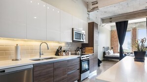 A modern kitchen with stainless steel appliances, a central island, and a view to a living area with a bed and a plant. - Downtown Dallas Gorgeous 3 BD, Pool & Gym (Dallas)