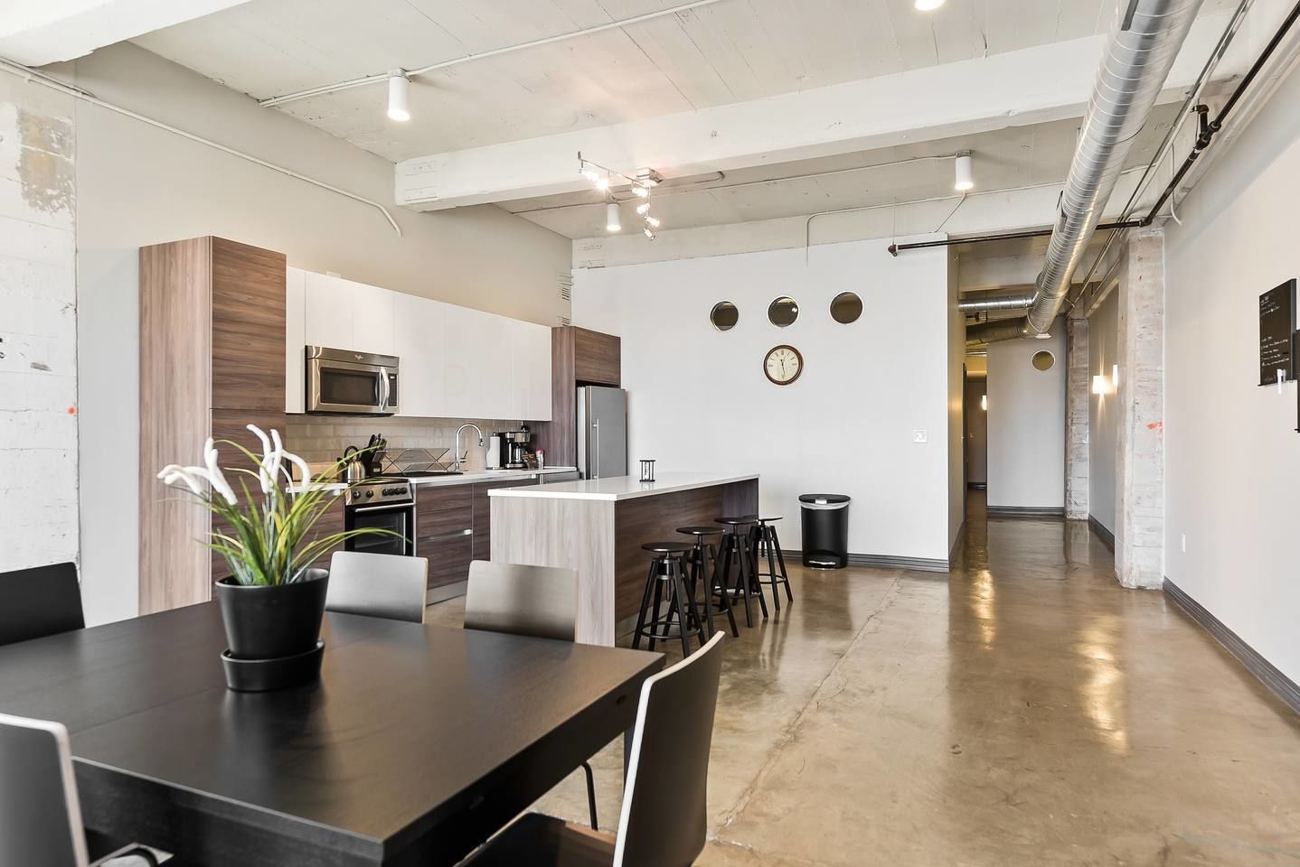 Una cocina moderna con una isla central, electrodomésticos de acero inoxidable y un comedor con mesa y sillas negras.