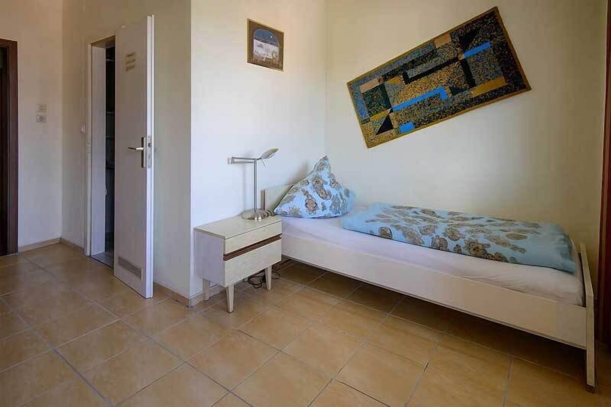 Un dormitorio con cama, mesita de noche, lámpara y un cuadro en la pared.