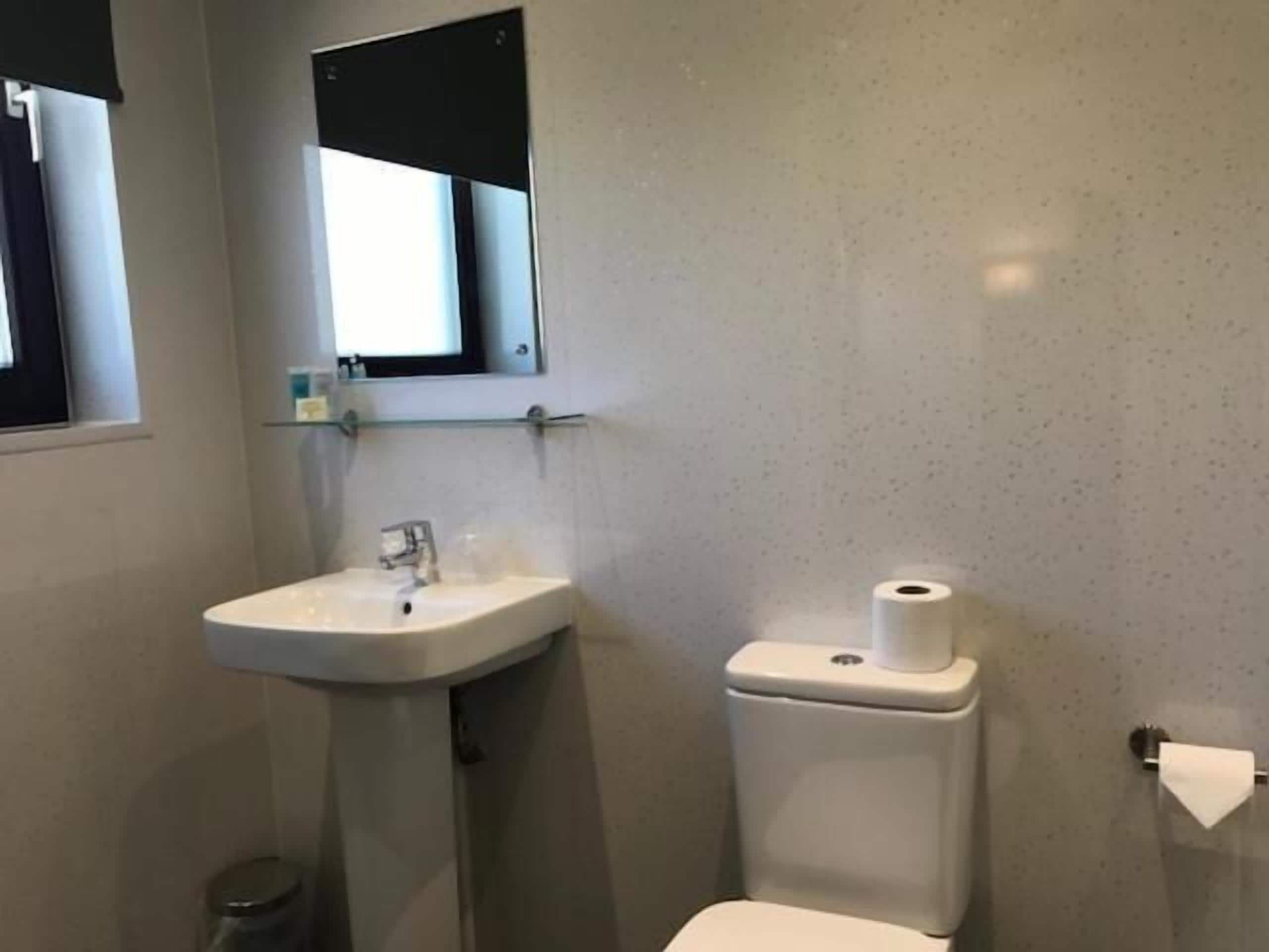 Un baño pequeño con un lavamanos blanco, un inodoro y un espejo sobre el lavamanos.