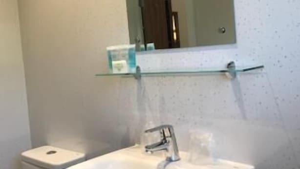 Un baño con un lavabo blanco, un espejo encima y un inodoro a la izquierda.