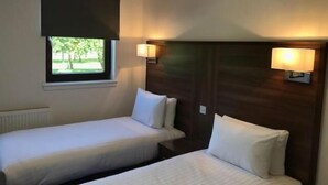 Habitación de hotel con dos camas individuales, ventana con vista a zonas verdes y lámparas fijadas a la pared.