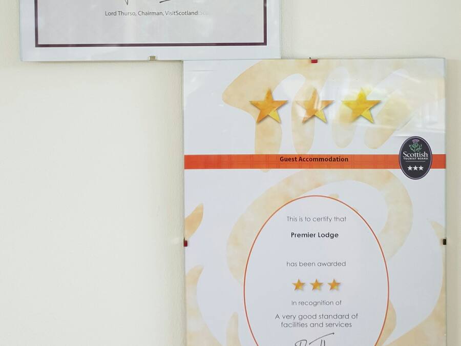 Two framed certificates: one for 'iKnow Scotland' as an Accredited Information Partner and another for 'Premier Lodge' as a Guest Accommodation with a three-star rating.