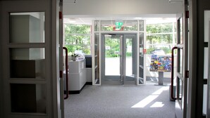 Un área de recepción con puerta de vidrio, mostrador de recepción y un tablón de anuncios con diversos avisos.