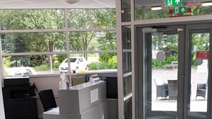Zona de recepción con mostrador, una impresora y una puerta de vidrio que da al exterior.