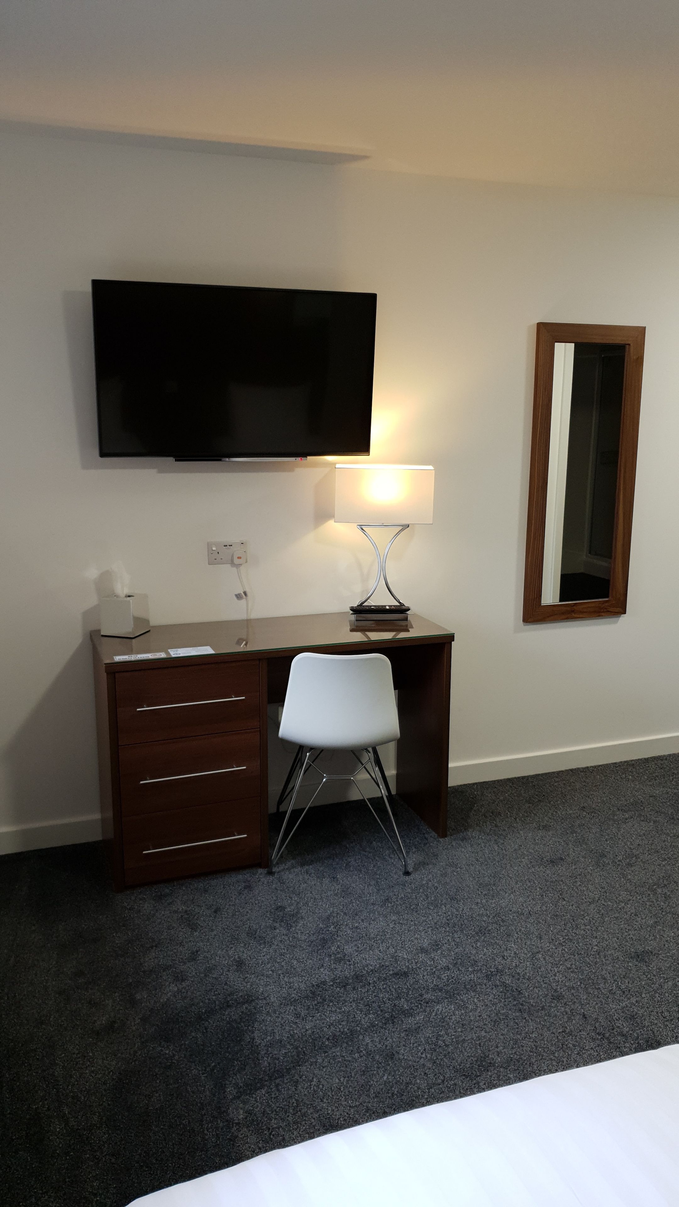 Une chambre d’hôtel comprenant un lit, un bureau avec une lampe, une télévision, un miroir et une chaise.