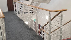 Una escalera moderna con barandilla de madera y pasamanos metálicos, que conduce a una habitación con una puerta que indica "Rooms 127-132".