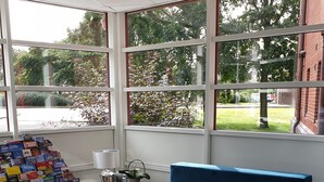 Una habitación moderna con ventanas amplias, un banco acolchado azul, una mesita con lámpara y una exhibición de folletos.