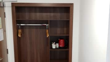 Una habitación con un armario de madera, un estante pequeño con una tetera roja y una alfombra gris.
