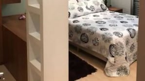 Um quarto com cama, mesa de cabeceira, prateleira na parede e um quadro.