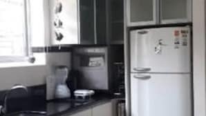 Cozinha com armários brancos, bancada preta, geladeira branca e uma janela.