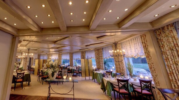 A dining area with multiple tables, chairs, and a chandelier. - Hotel & Restaurant Zur Windmühle (Beckum)