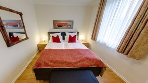 A neatly made bed with a red and white bedspread, two bedside lamps, a large mirror, and a window with curtains. - Hotel & Restaurant Zur Windmühle (Beckum)