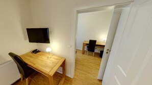 A small, tidy room with a wooden desk, a chair, a television mounted on the wall, and a door leading to another room. - Hotel & Restaurant Zur Windmühle (Beckum)