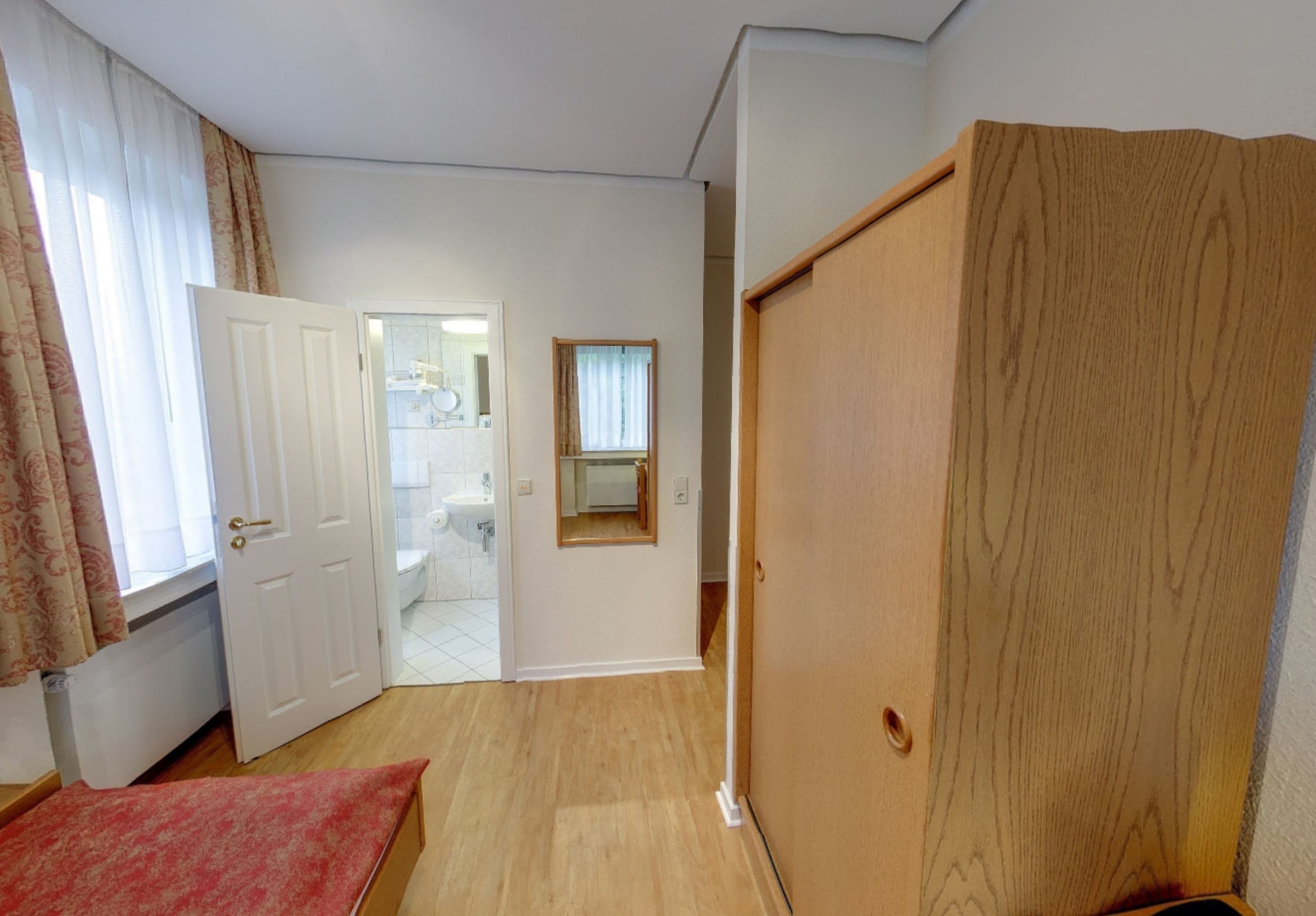 Una habitación con un armario de madera, una puerta que da al baño y una alfombra roja en el suelo.