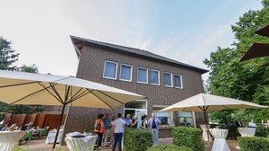 An outdoor patio area with tables and umbrellas, a brick building in the background, and well-maintained greenery. - Hotel & Restaurant Zur Windmühle (Beckum)