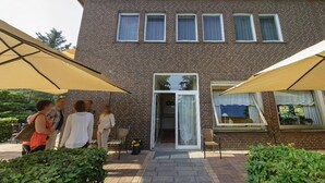 A brick building with a glass door entrance, outdoor seating area, and large umbrellas. - Hotel & Restaurant Zur Windmühle (Beckum)