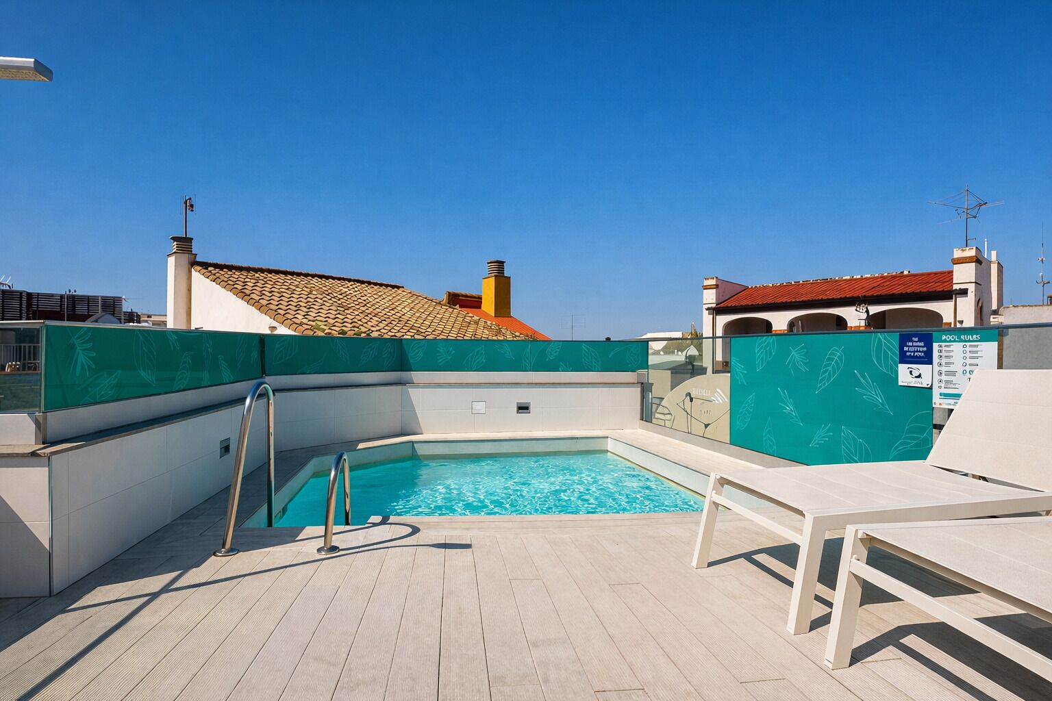 A rooftop pool with clear blue water, surrounded by a wooden deck and white lounge chairs.