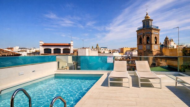 A rooftop pool with clear blue water, lounge chairs, and a historic tower in the background. - Numa Seville Molina (Seville)