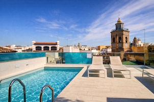 A rooftop pool with clear blue water, lounge chairs, and a historic tower in the background.