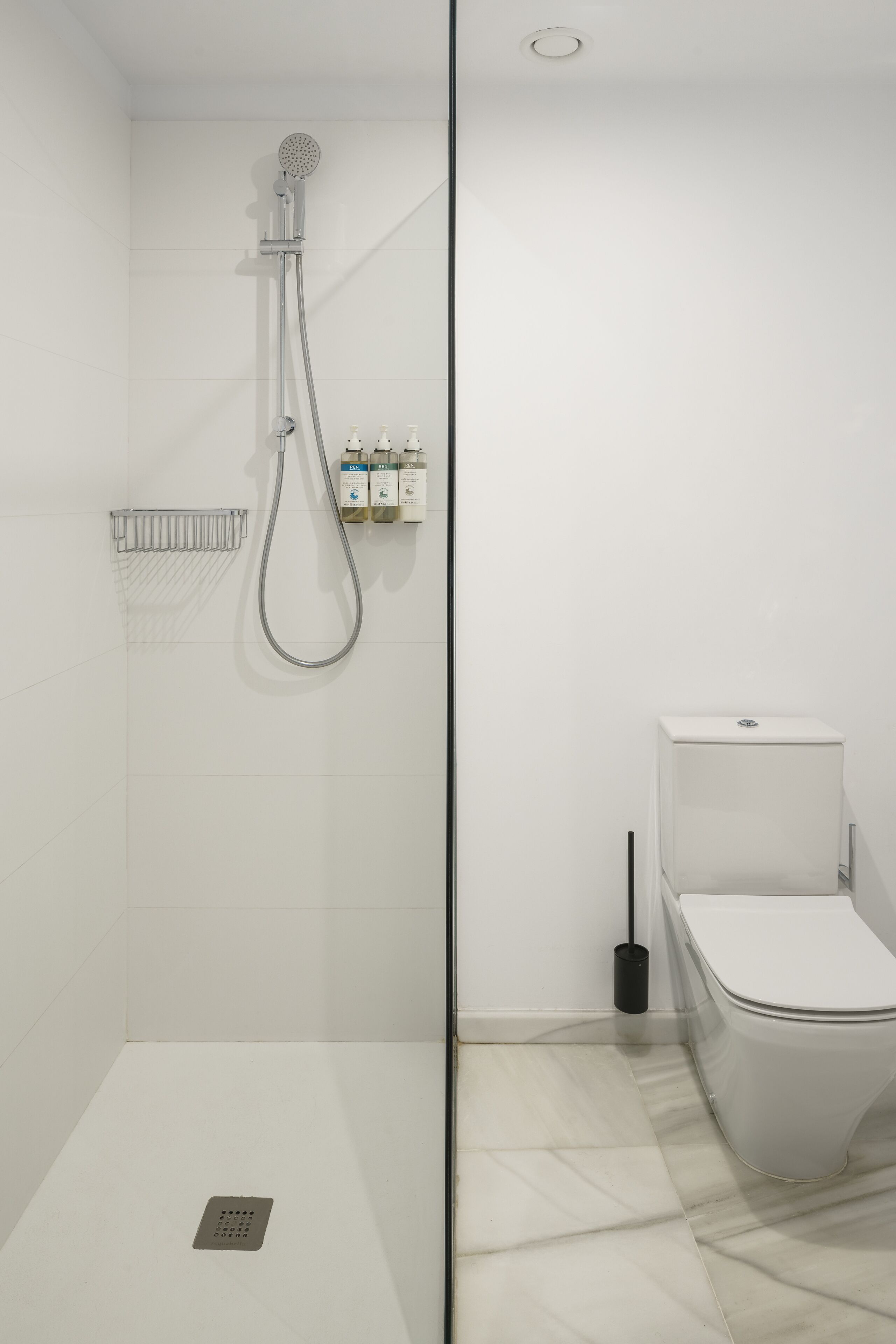 Une salle de bain moderne dotée d’une douche à parois de verre, de toilettes et d’un sèche-mains.