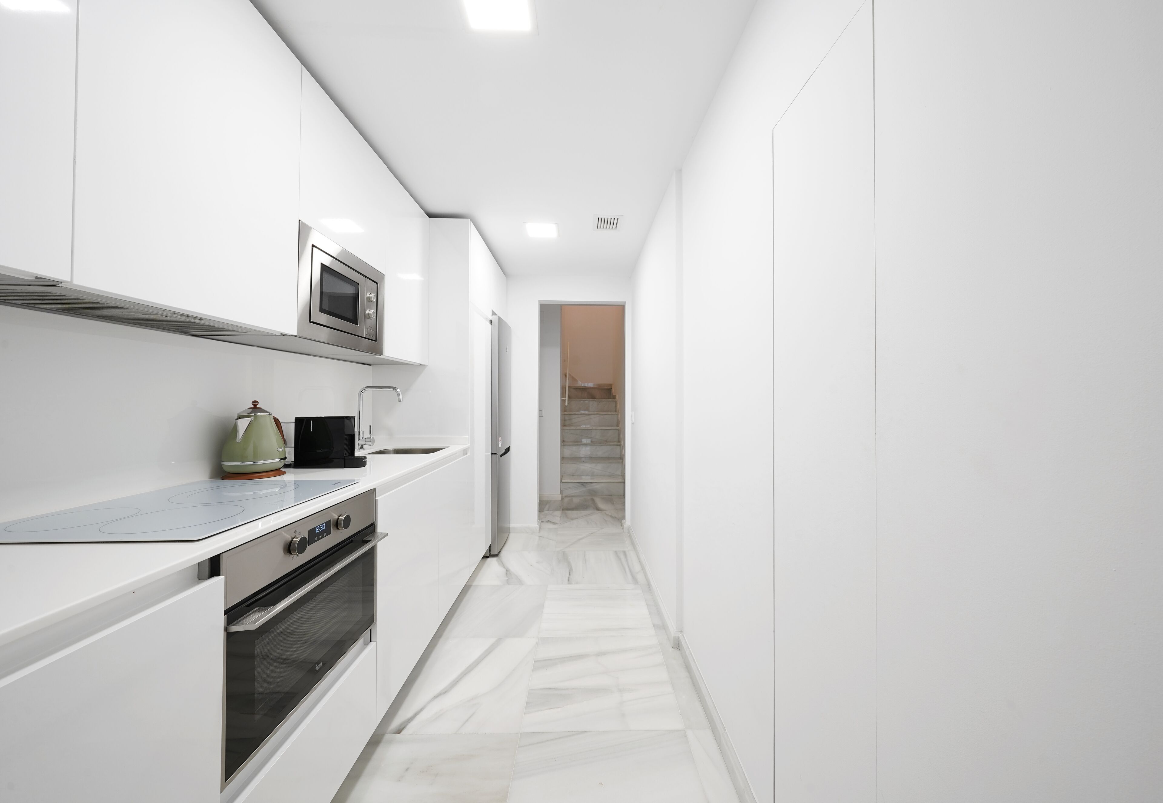 A narrow kitchen with white cabinetry, a built-in oven, and a microwave.