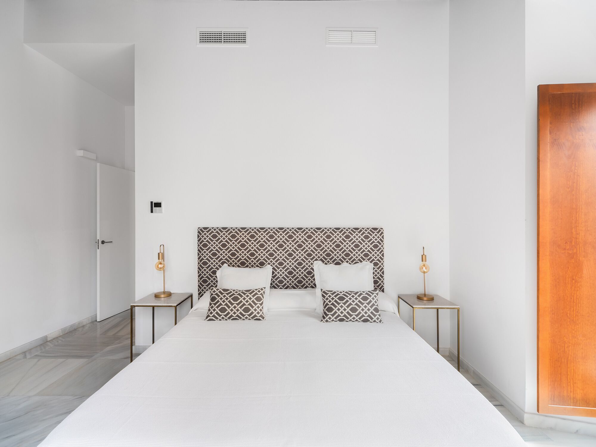 Een moderne hotelkamer met een groot bed, twee nachtkastjes met lampen, een gestreept hoofdbord en een houten deur.
