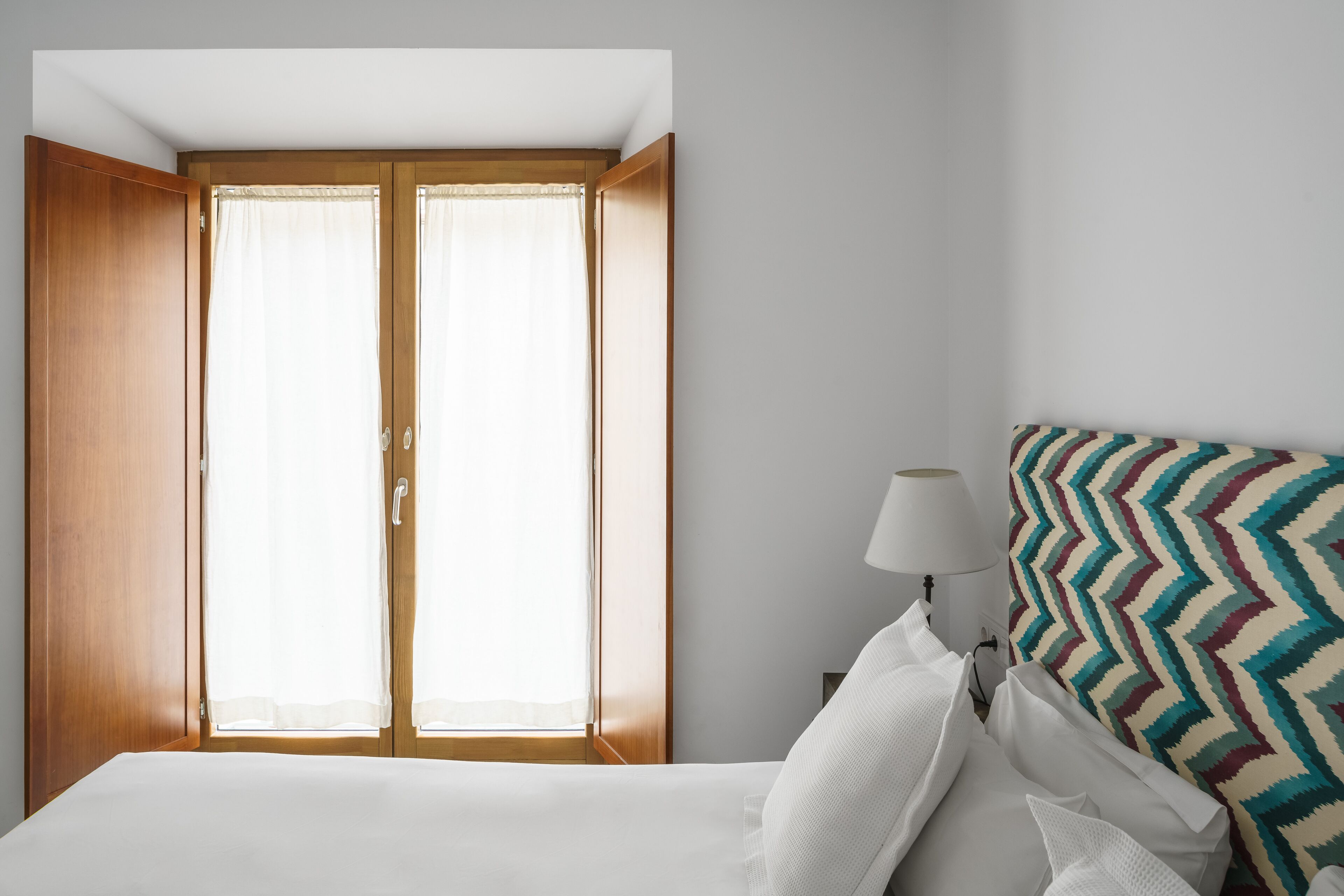 Una camera da letto con un letto, un comodino, una lampada, una testiera a motivi decorativi e un armadio in legno con una finestra.