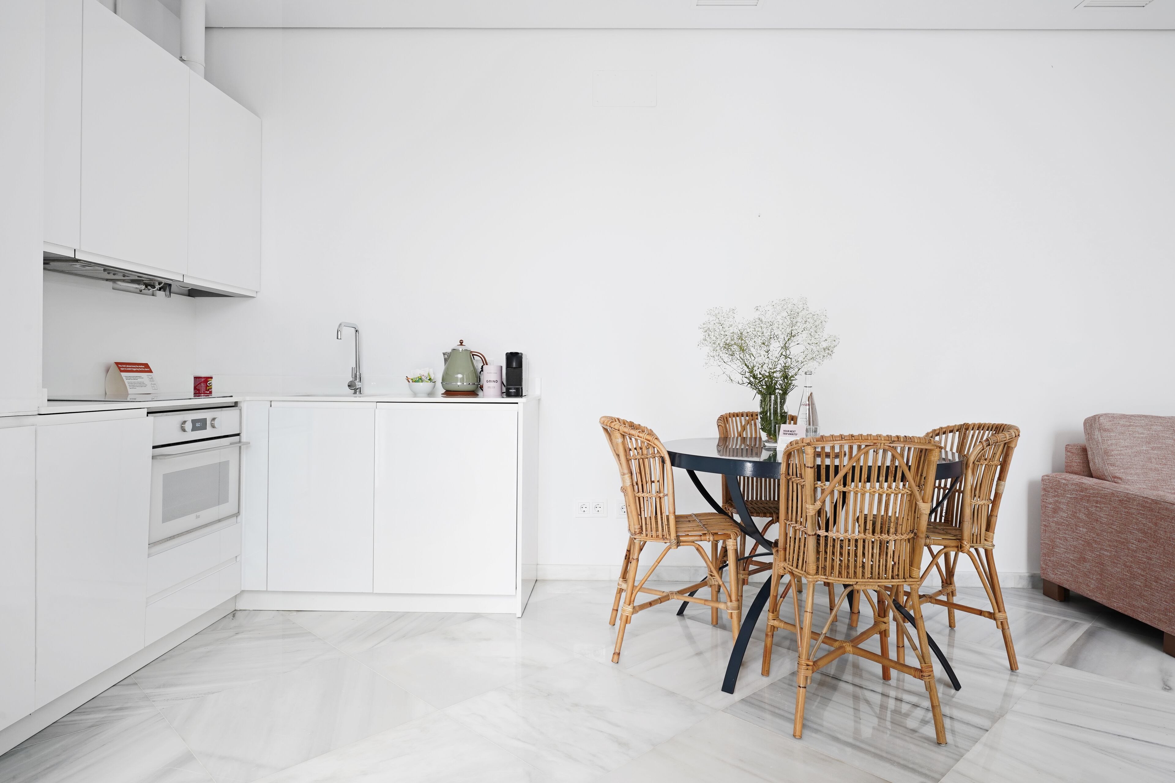 Eine moderne Küche mit weißen Schränken, einem eingebauten Backofen und einem Essbereich mit Tisch und Korbstühlen.