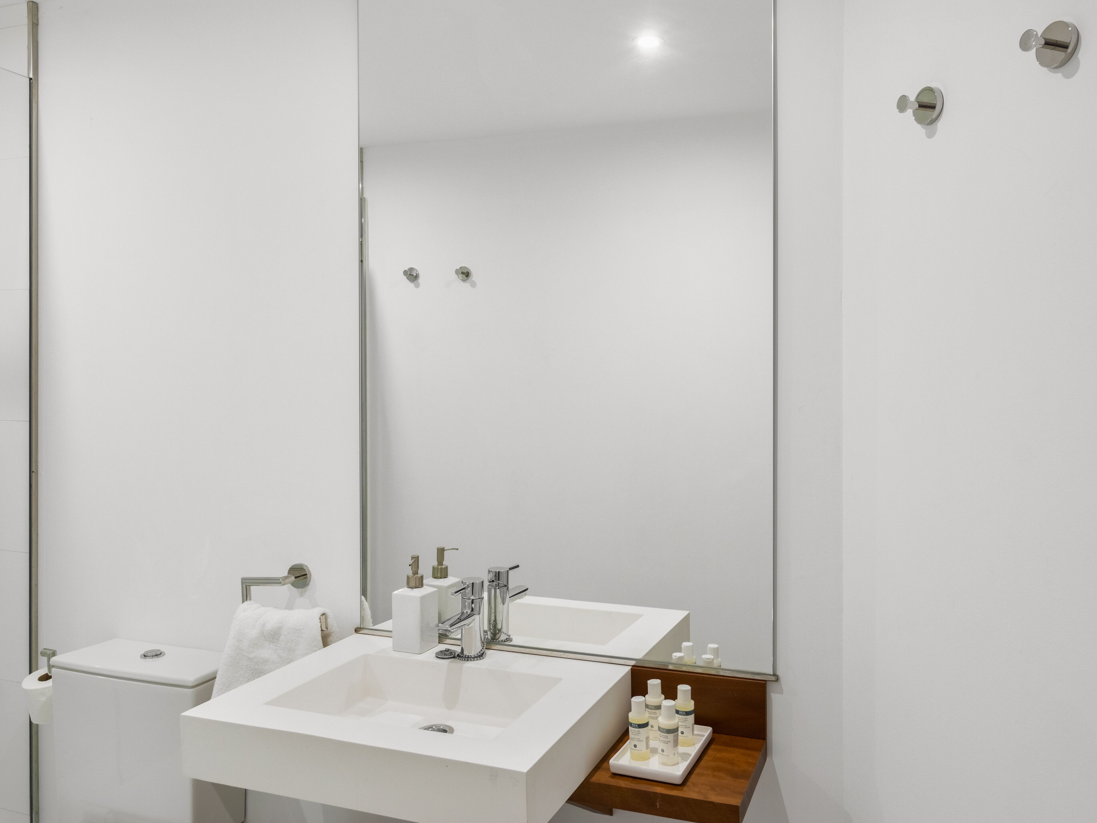 A modern bathroom with a large mirror, two sinks, and a toilet.