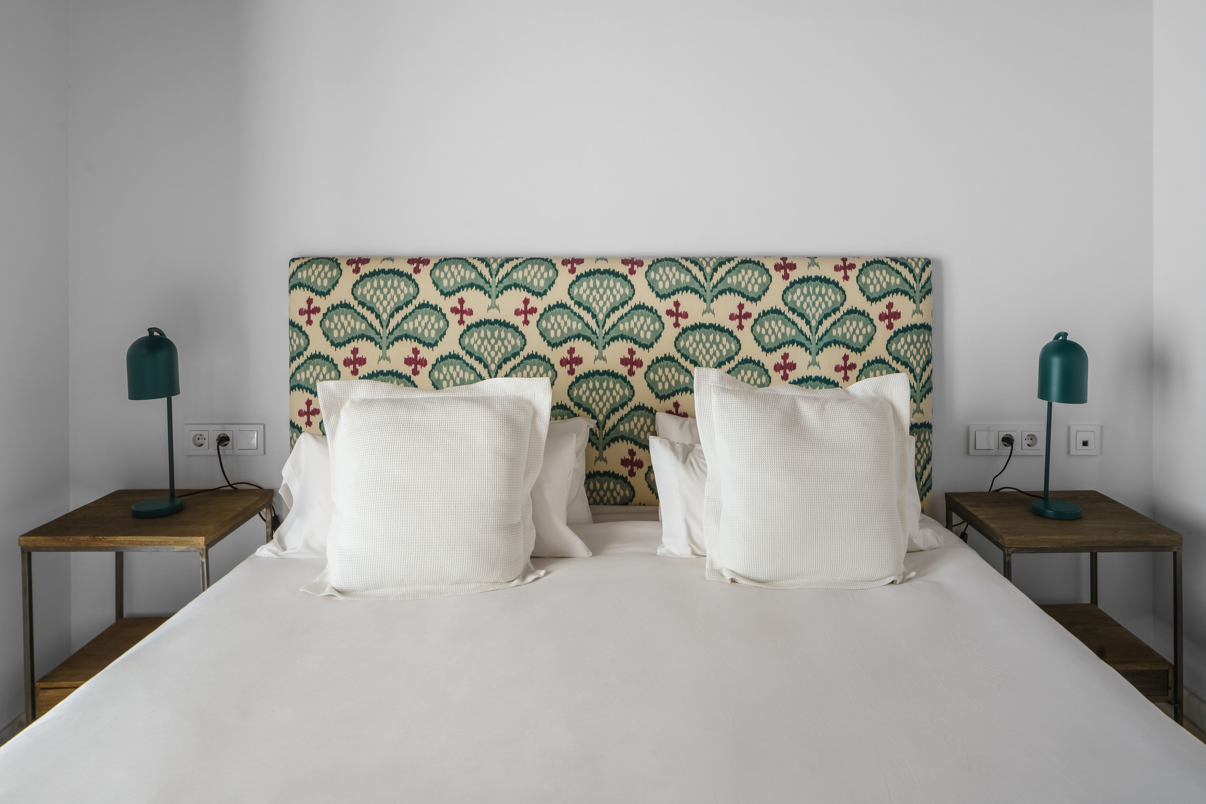 A neatly made bed with white linens, two bedside tables with lamps, and a patterned headboard.