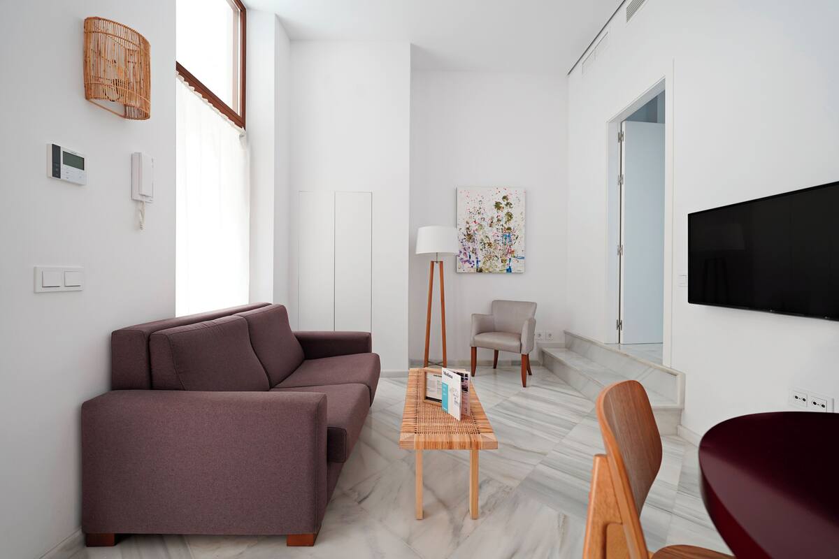 A modern living room with a sofa, a wooden coffee table, a chair, a TV, and a painting on the wall.