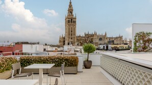 A rooftop terrace with a table and chairs, a potted tree, and a view of a historic cathedral. - Numa Seville Molina (Seville)