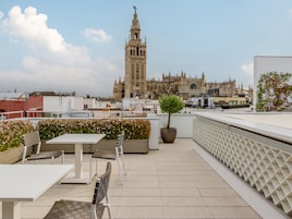 A rooftop terrace with a table and chairs, a potted tree, and a view of a historic cathedral.