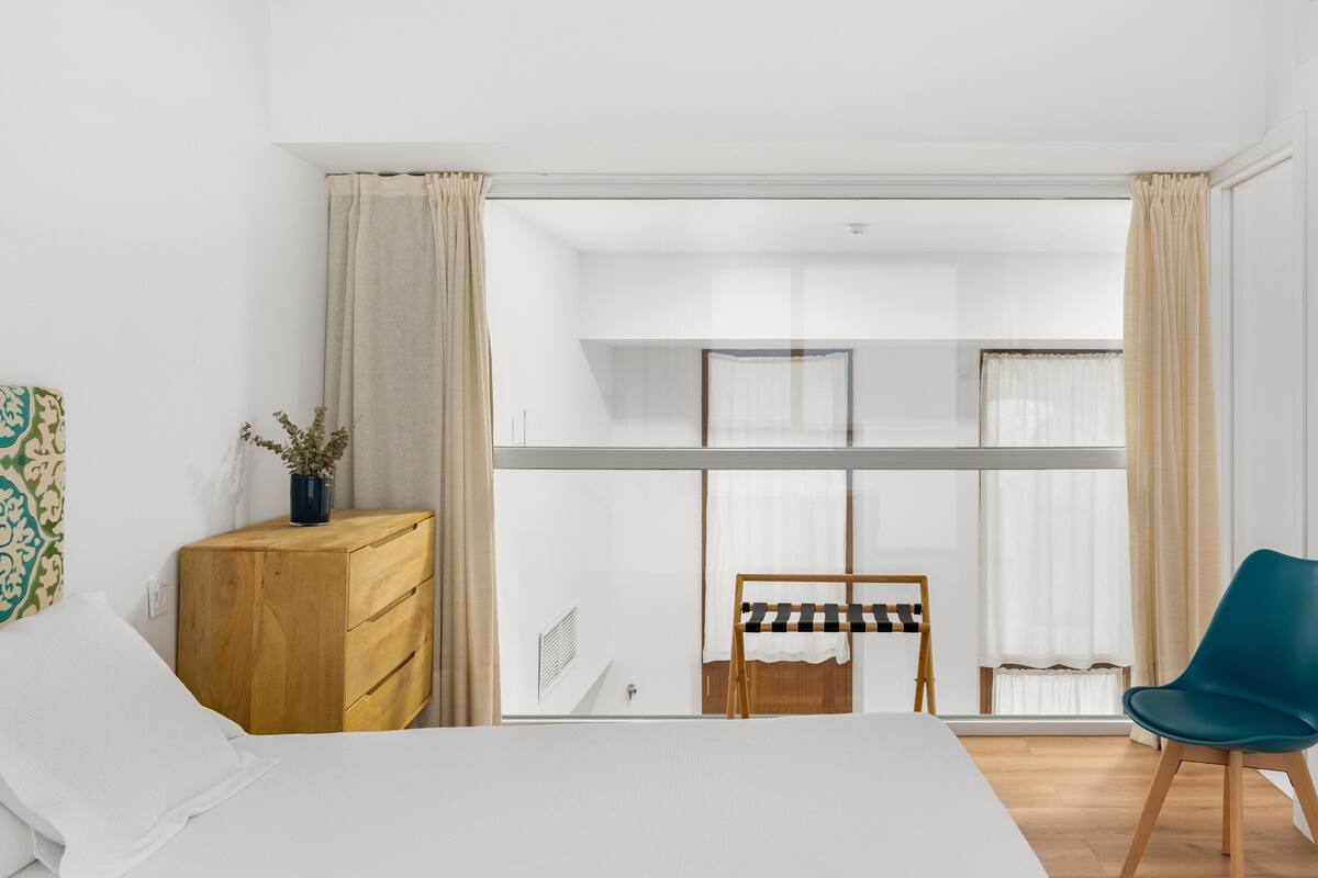 A modern bedroom with a bed, a wooden dresser, a chair, and a window with curtains.