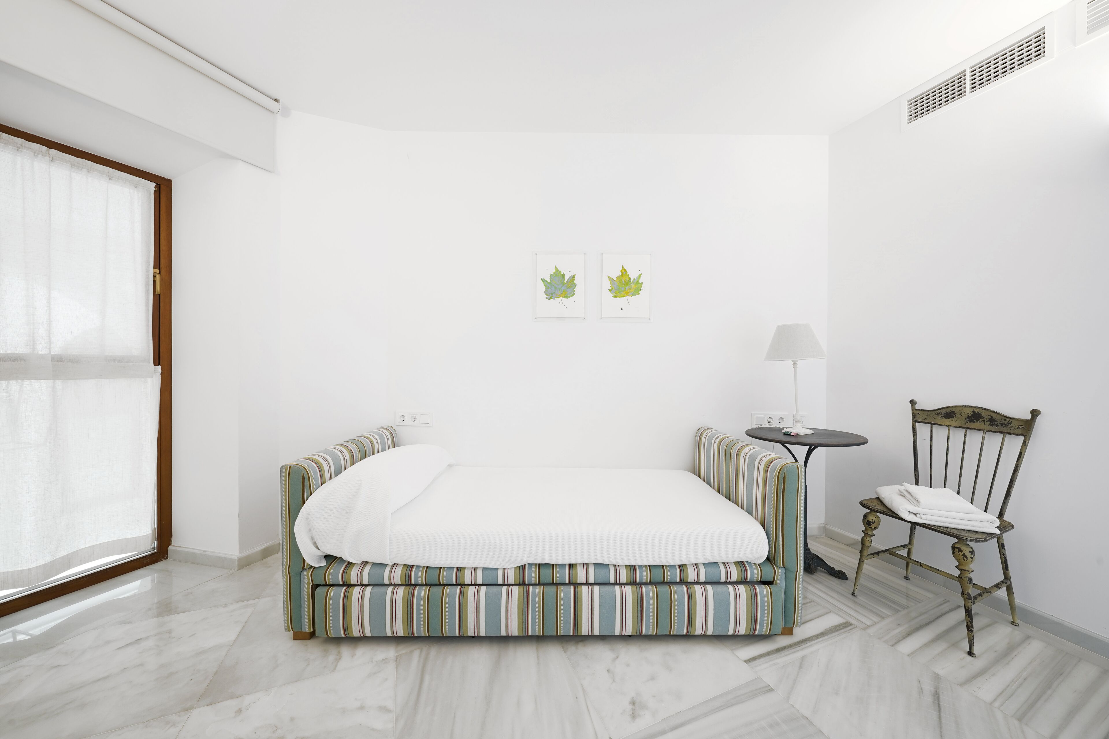 Une chambre à coucher comprenant un lit, une chaise, une petite table et deux œuvres d’art murales.