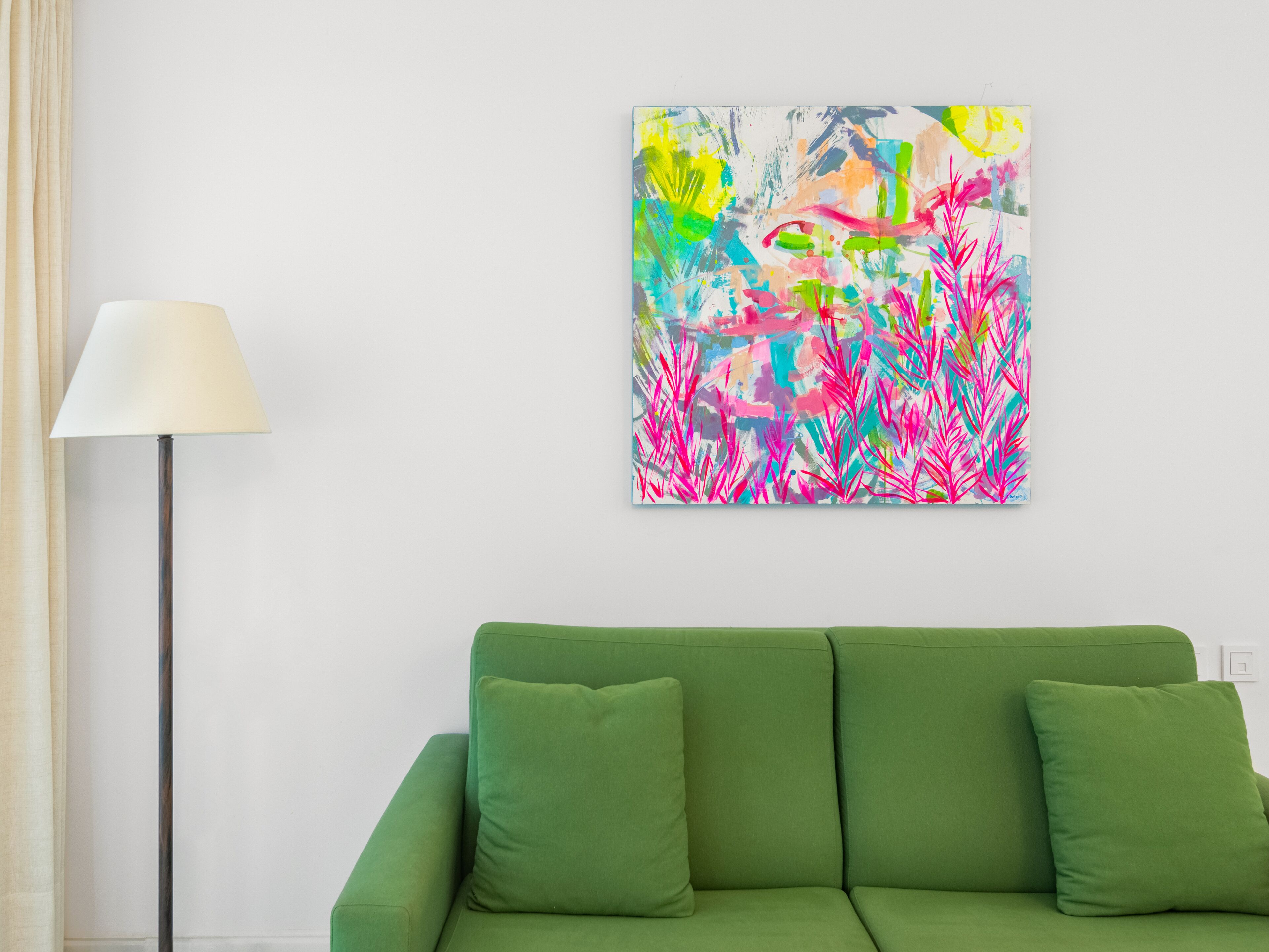 A green sofa with cushions, a floor lamp, and a colorful abstract painting on the wall.