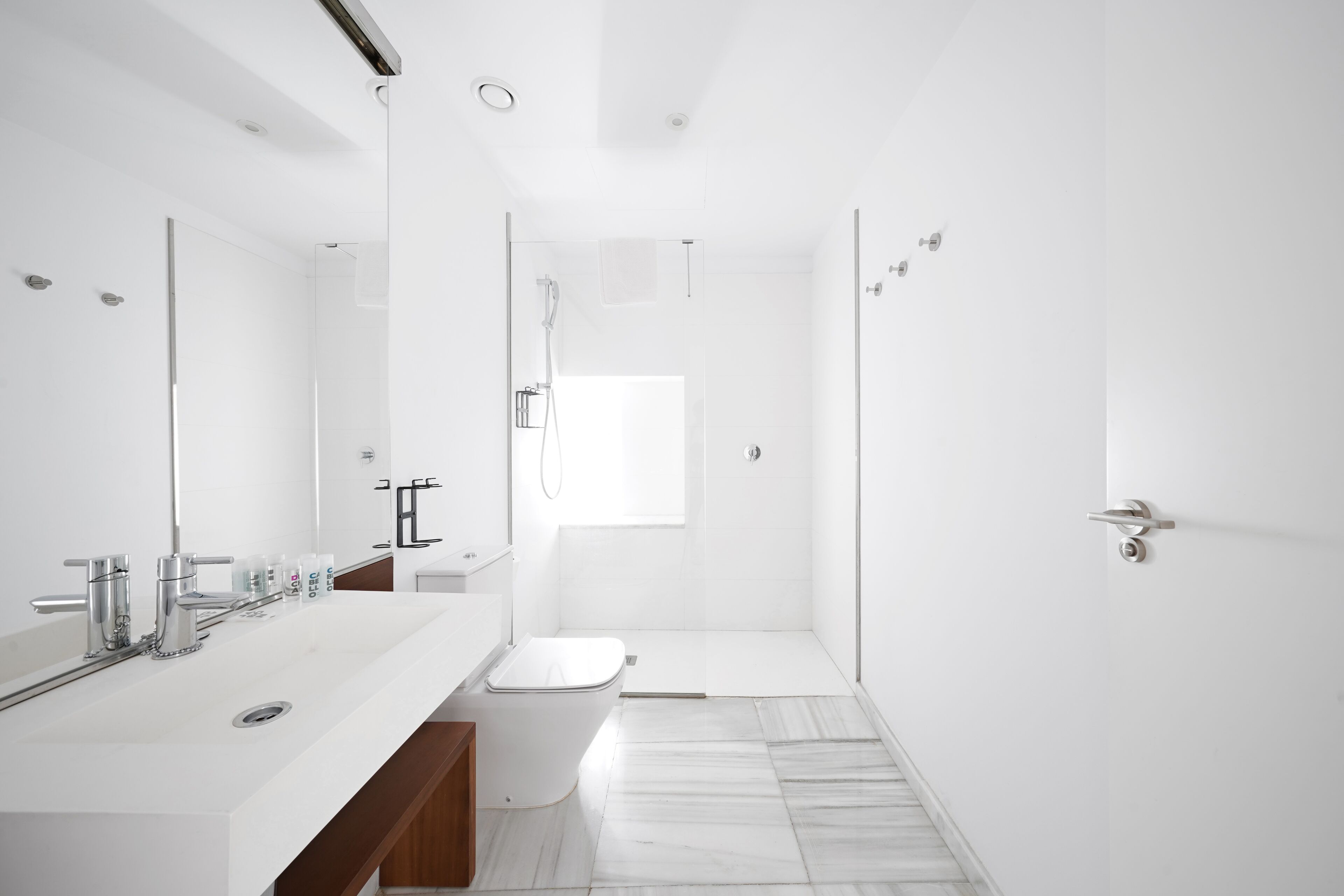A modern bathroom with a large mirror, a white sink, a toilet, and a shower area.