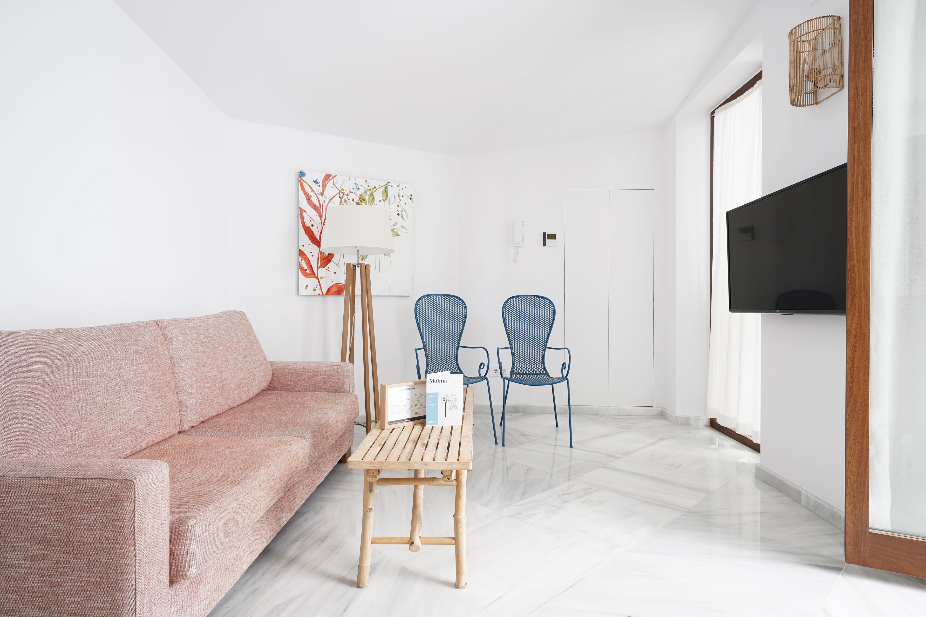 Una sala de estar moderna con un sofá, dos sillones, una mesita de madera, una lámpara de pie y un televisor.