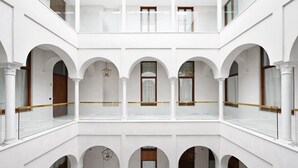 A multi-level courtyard with white walls and arches, featuring balconies and hanging light fixtures. - Numa Seville Molina (Seville)