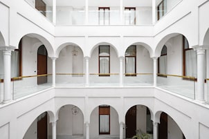 A multi-level courtyard with white walls and arches, featuring balconies and hanging light fixtures.