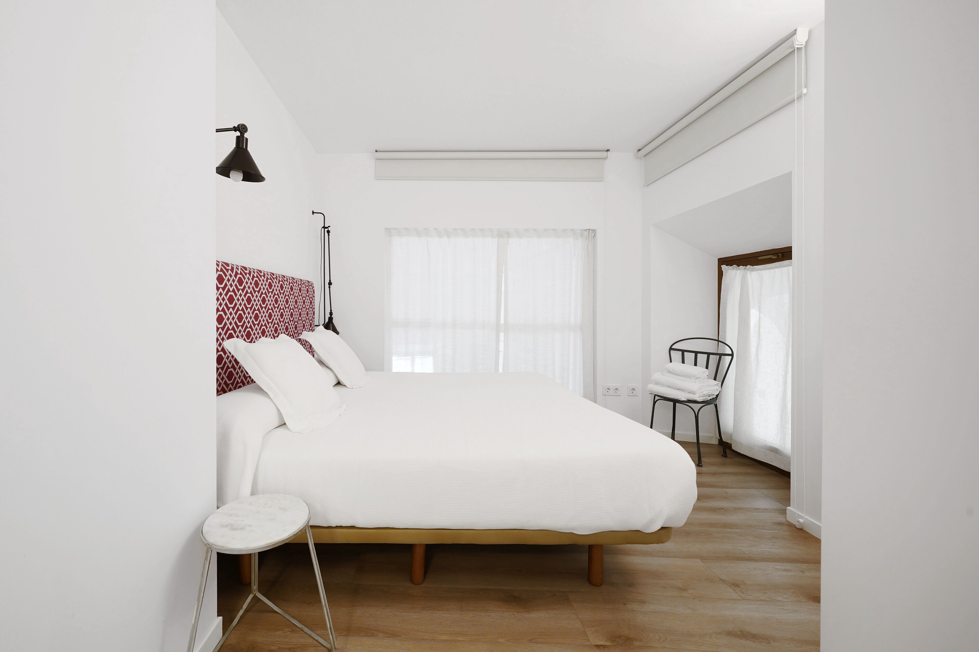 A bedroom with a bed, a bedside table, a chair, a floor lamp, and a window with curtains.