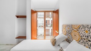 A modern bedroom with a large bed, a wooden door, and a view of the outside. - Numa Seville Molina (Seville)