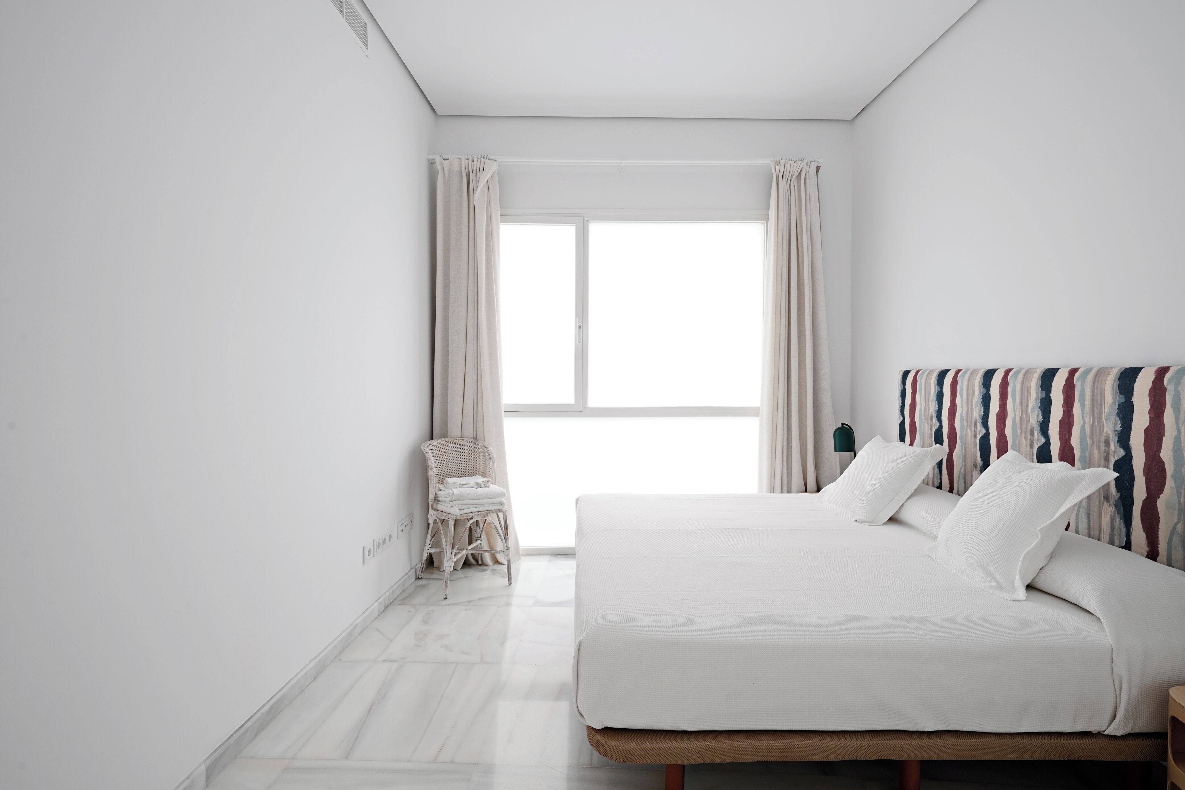 Un dormitorio minimalista con una cama grande, una silla y vistas al exterior a través de una ventana.