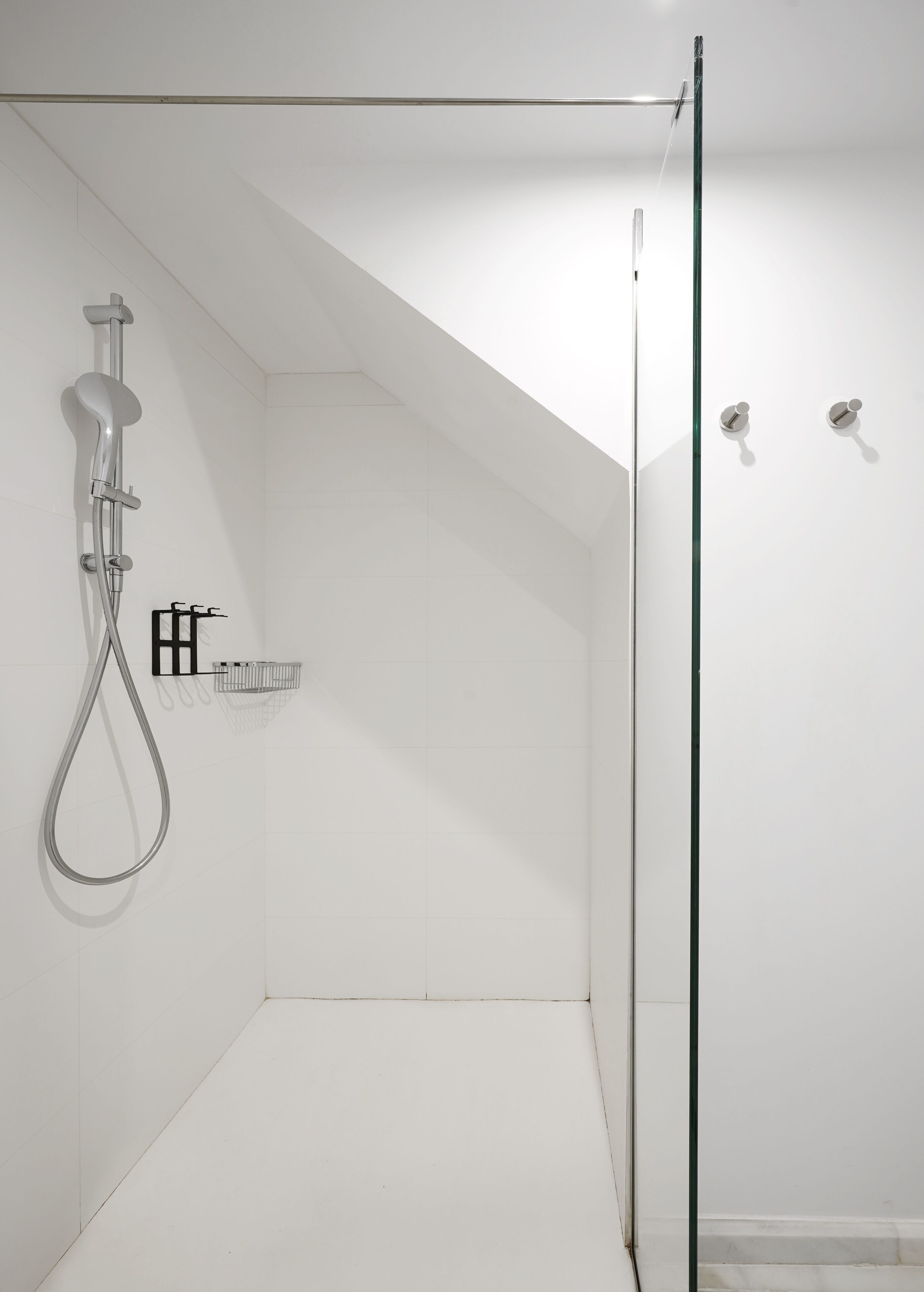 A modern shower with a glass door, a handheld showerhead, and a black towel rack.