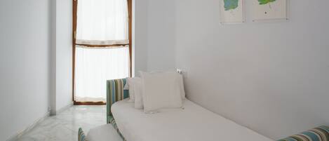 A bedroom with a bed, a bench, a window with curtains, and two framed leaves on the wall.