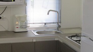 A compact kitchen with a microwave, coffee maker, sink, and gas stove.
