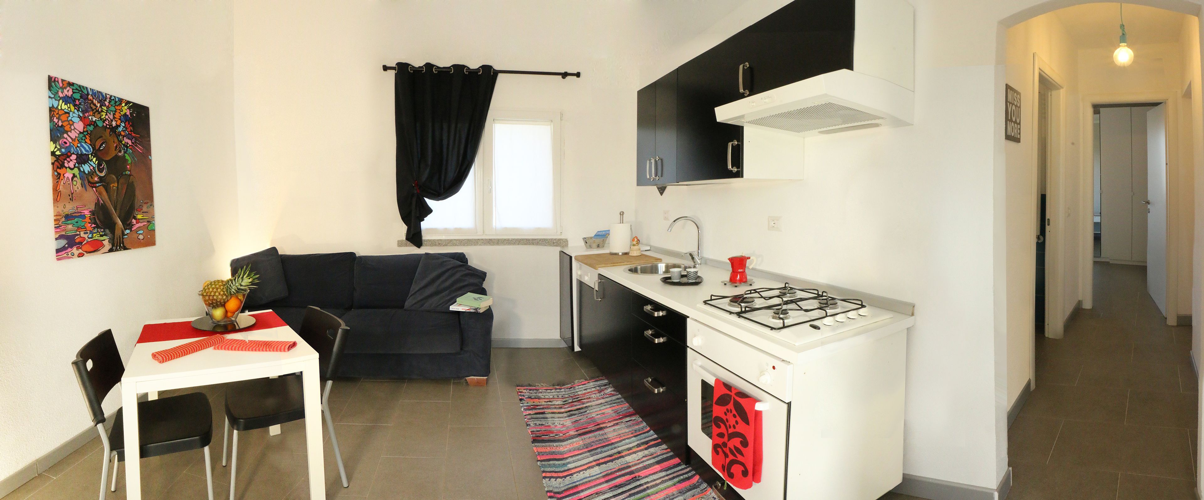 A compact kitchen with a dining area, a black sofa, and a colorful artwork on the wall.
