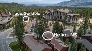 An aerial view of Village Gondola and Helios N5 buildings with surrounding greenery and a mountain backdrop.